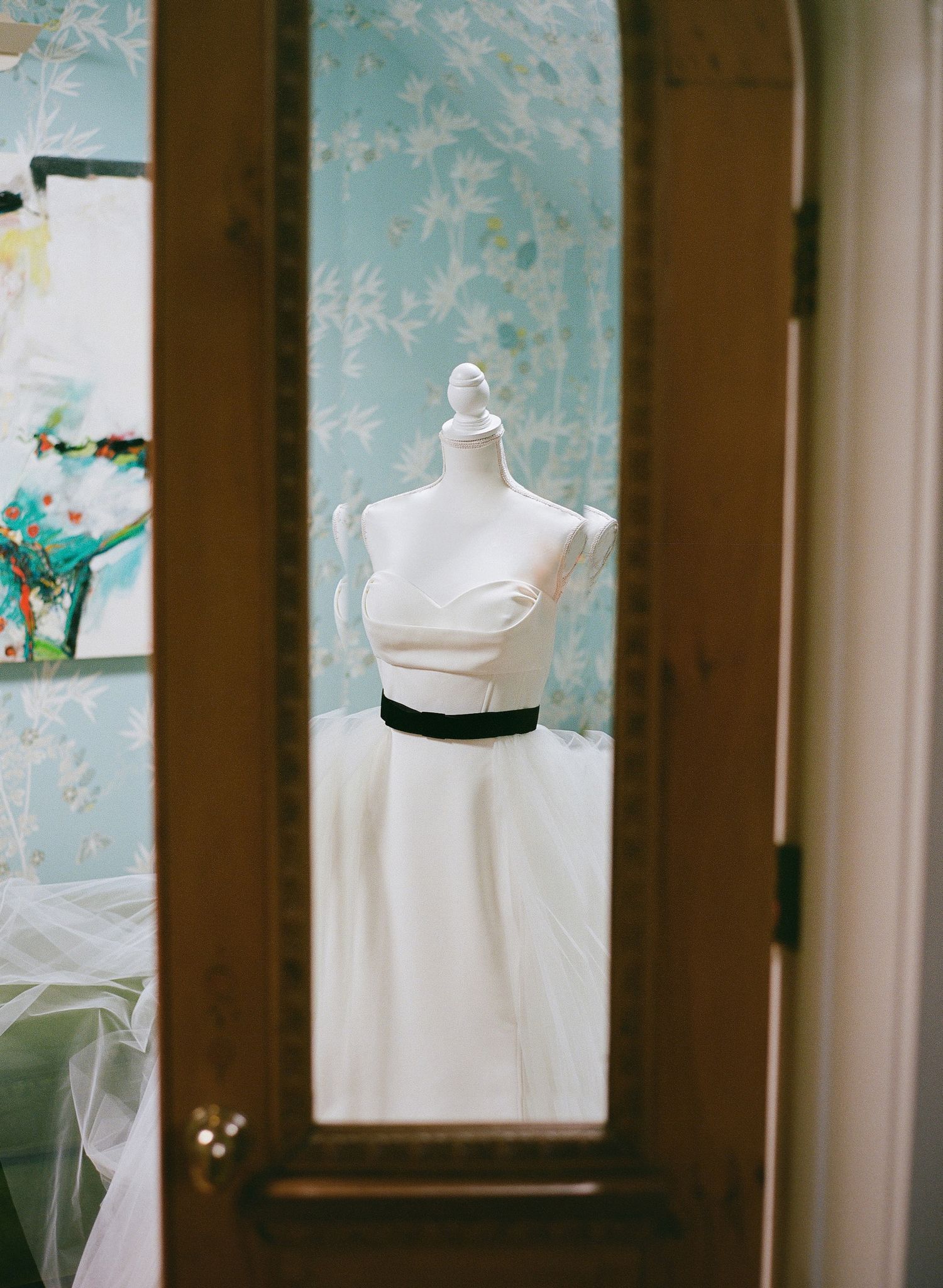 White wedding dress bodice on mannequin reflected in mirror with blue floral wallpaper.