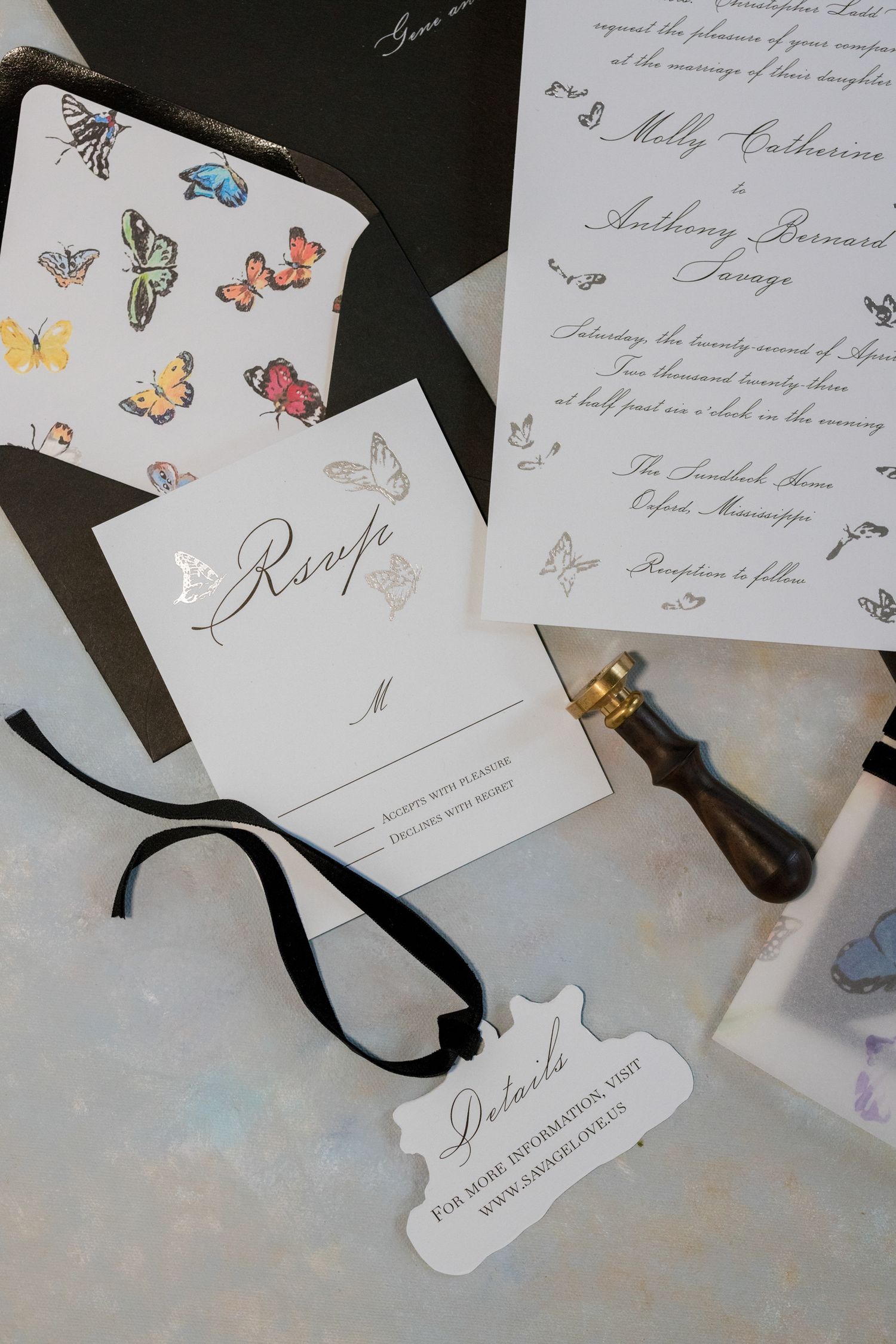 Wedding stationery featuring delicate butterfly designs, calligraphy and a black ribbon on a light marble surface.