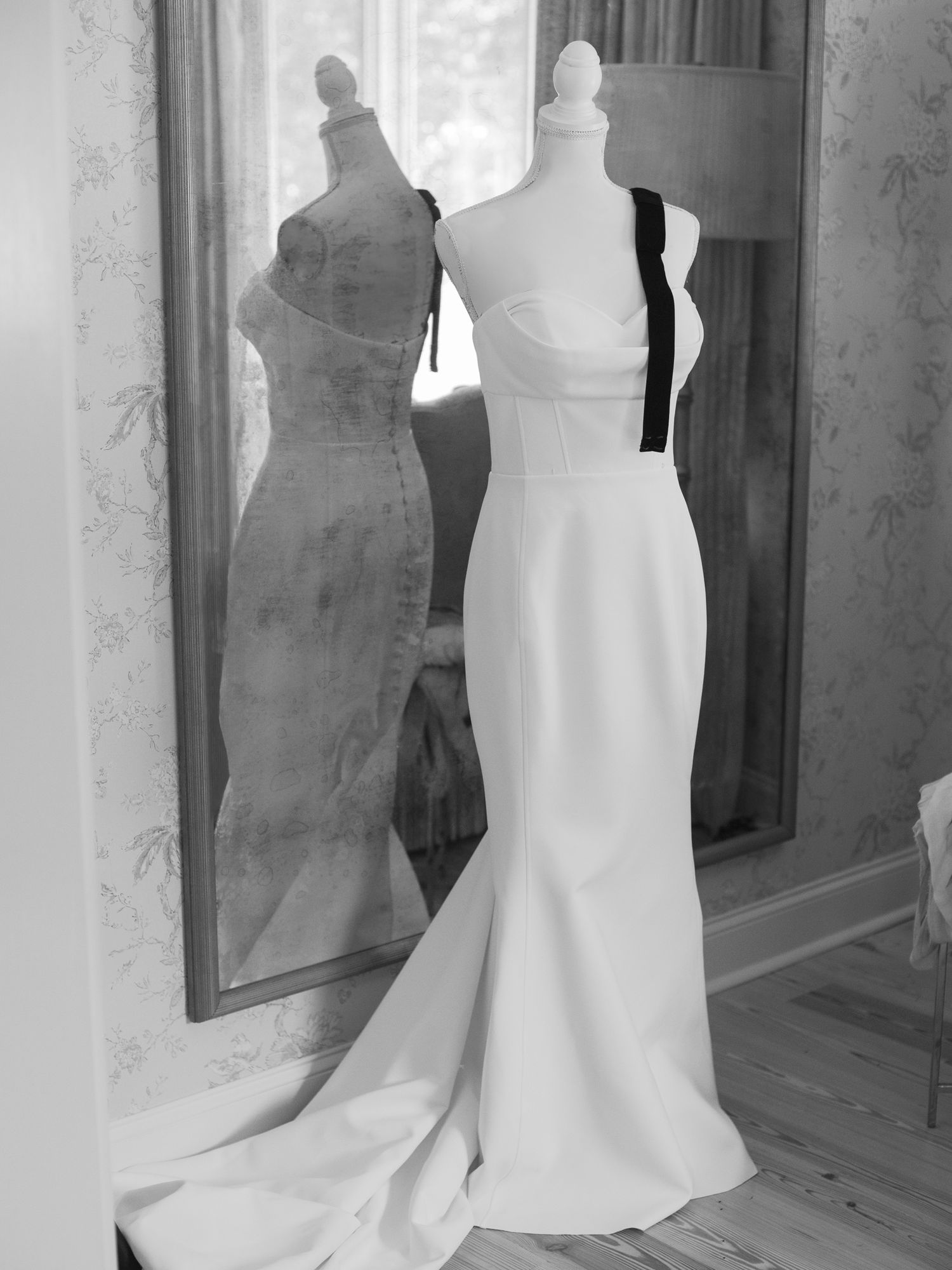 Elegant white wedding gown with fitted silhouette displayed next to mirror in black and white.
