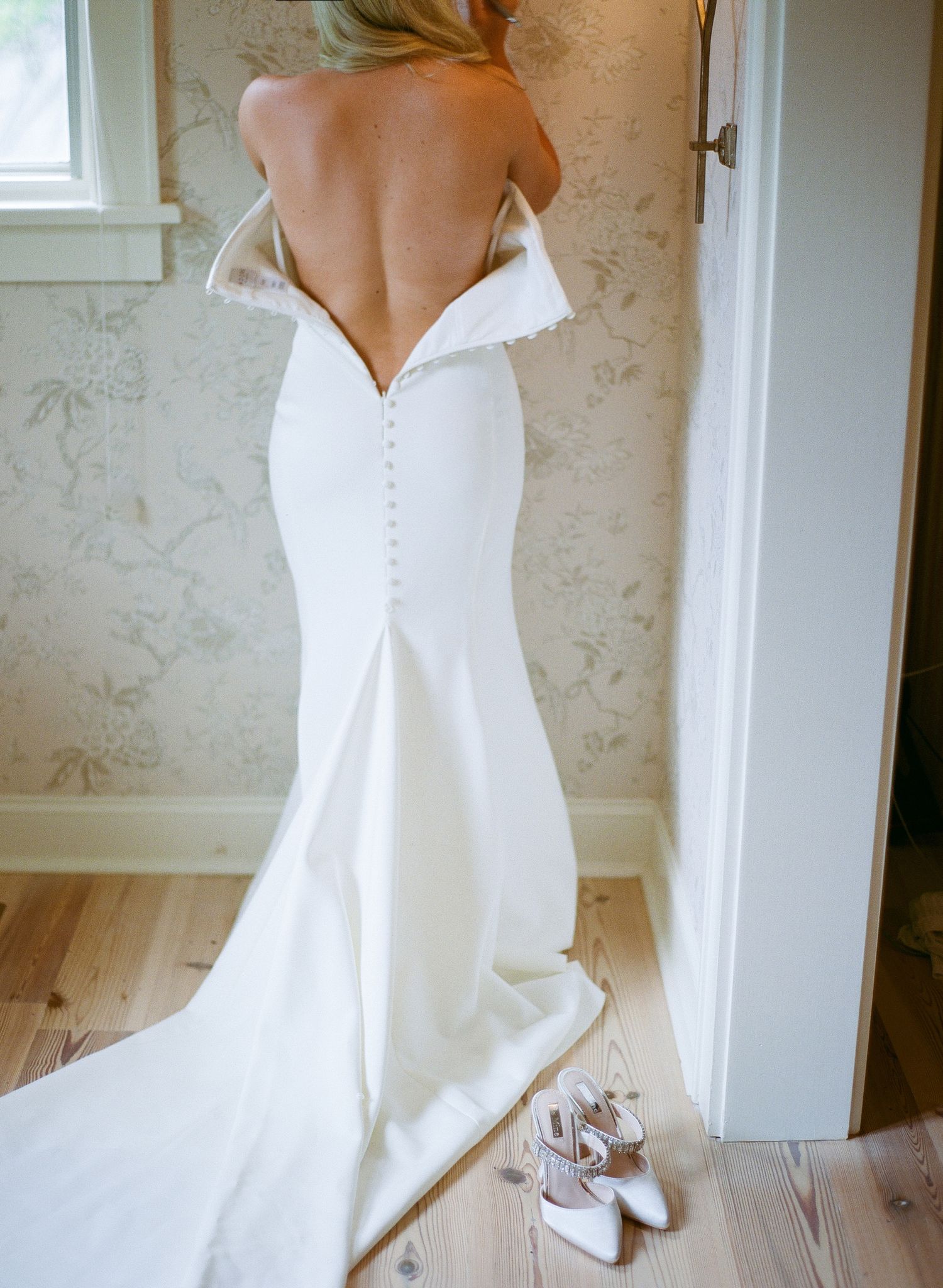 Dramatic backless wedding gown with button details and train displayed with white heels.