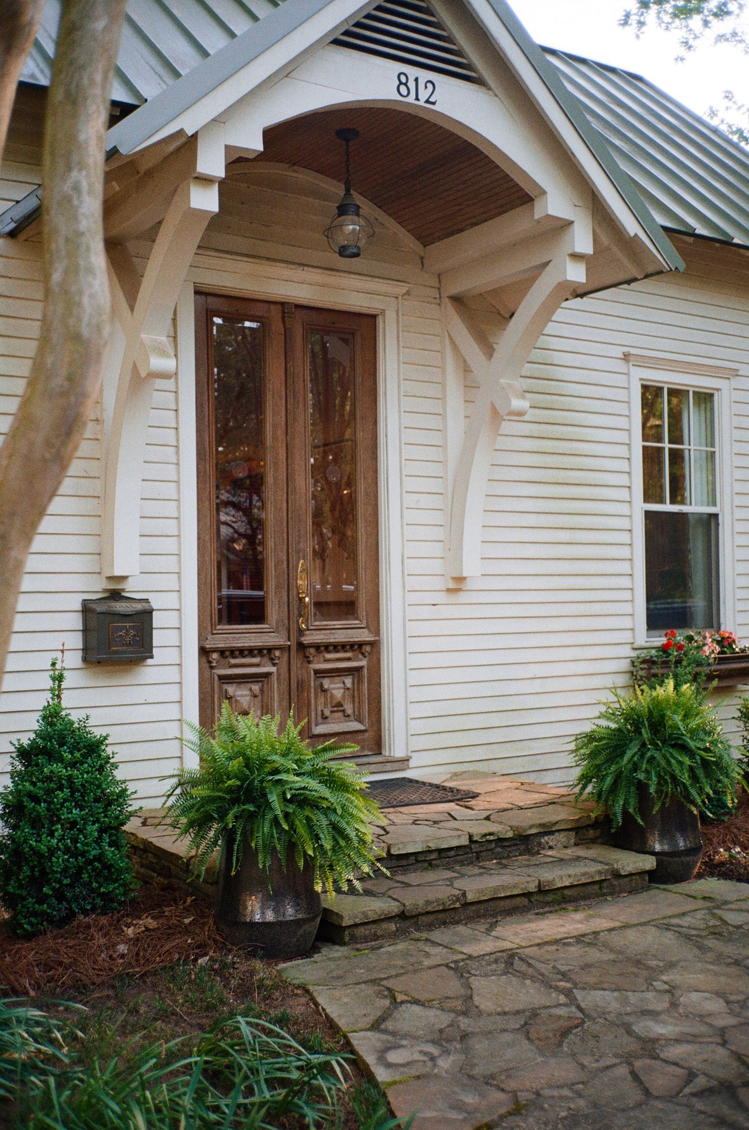 Charming cottage entrance with wooden screen door, ornate trim, and potted ferns at address 812.