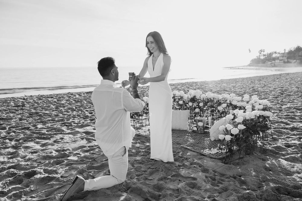A romantic beach proposal at sunset with white floral decorations on the sand.