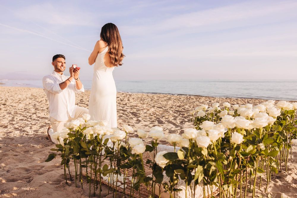 A beachside proposal moment decorated with white flowers during golden hour.