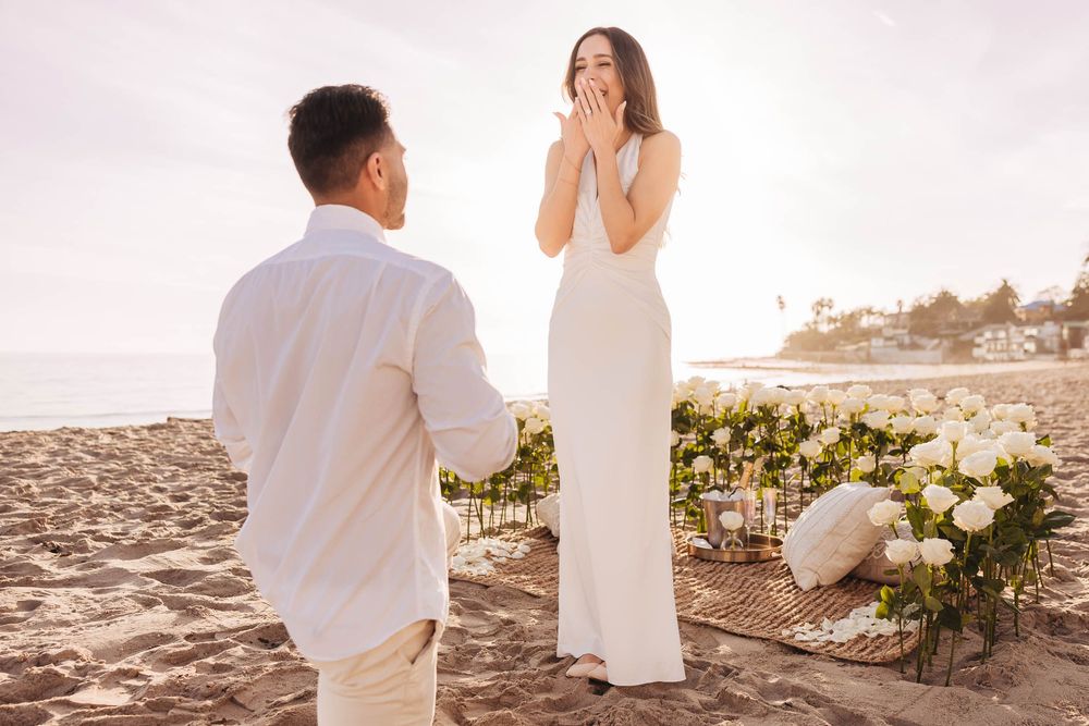 A joyful reaction during a surprise beach proposal with floral decorations.