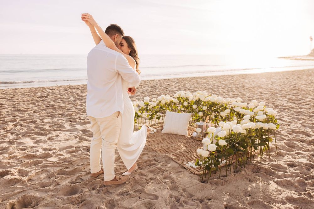 A romantic dance moment on the beach with sunset and floral arrangements.