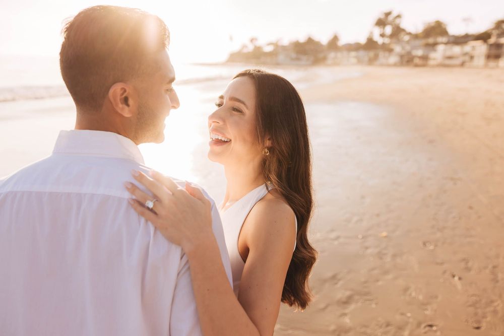 Romantic beach engagement photos with couple in white outfits during golden hour.