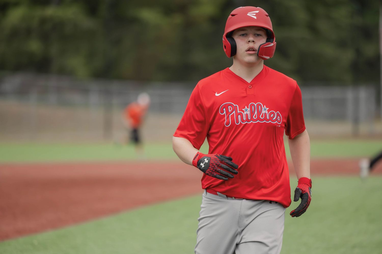 Baseball player in red Phillies uniform running on field during game.