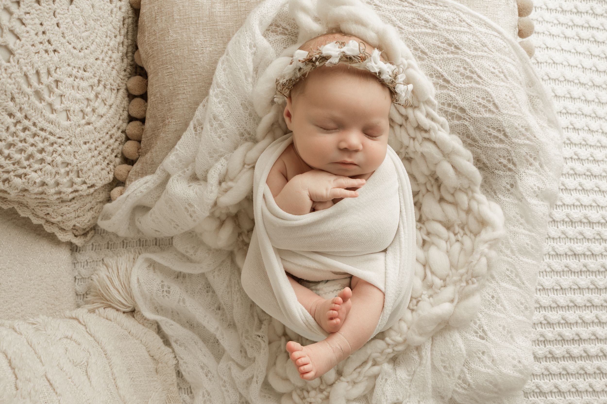 Sleeping newborn wrapped in cream colored swaddle blanket on textured white bedding.