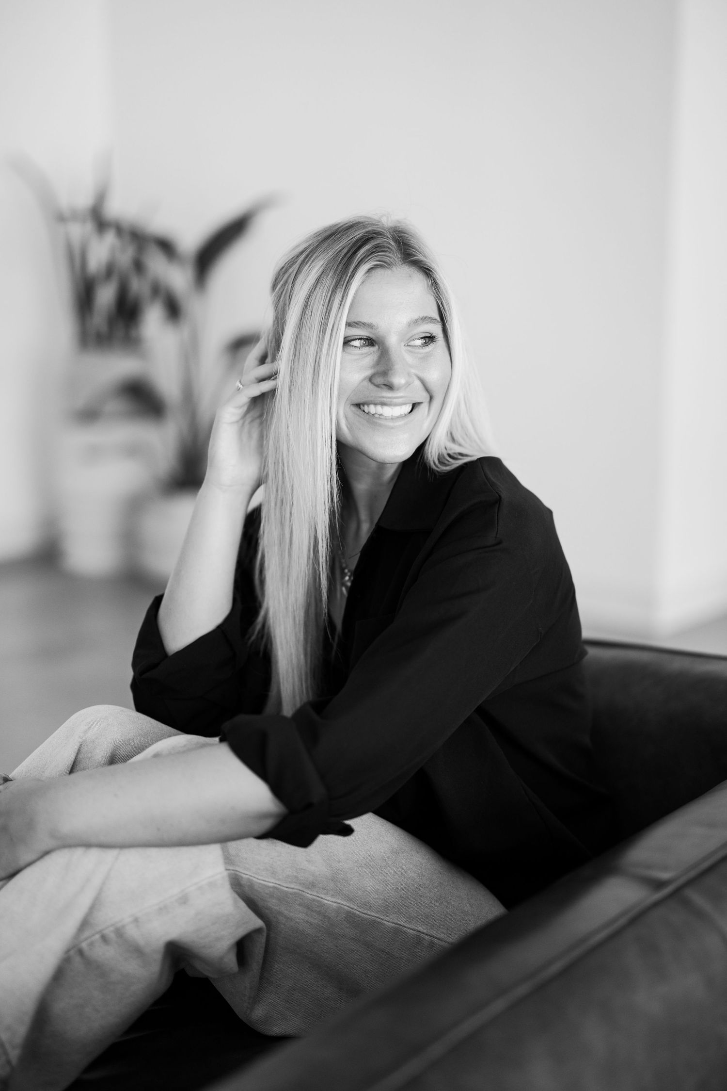 Black and white portrait of a joyful woman with blonde hair lounging on sofa.