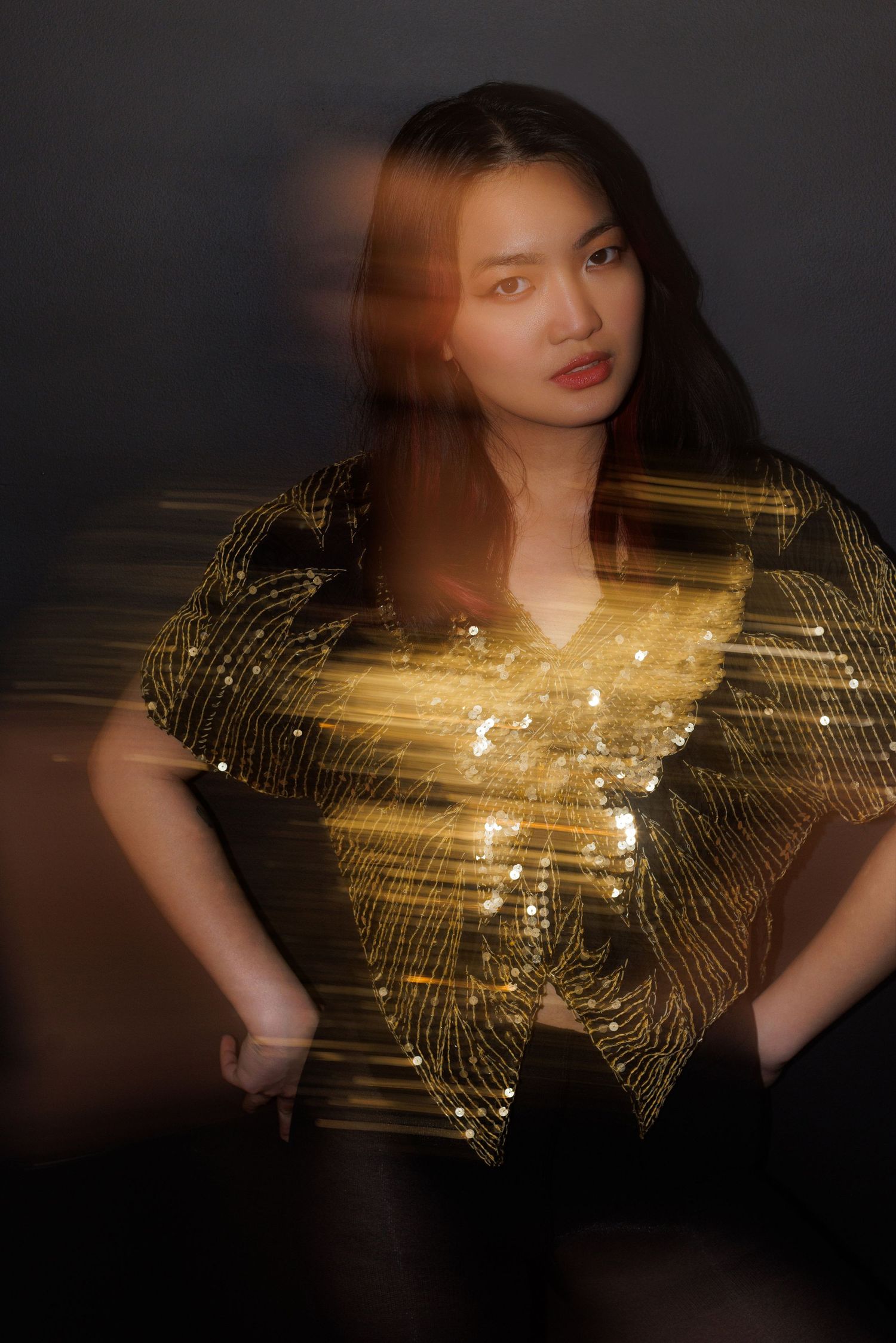 Fashion portrait in gold sequined top with artistic motion blur against black background.
