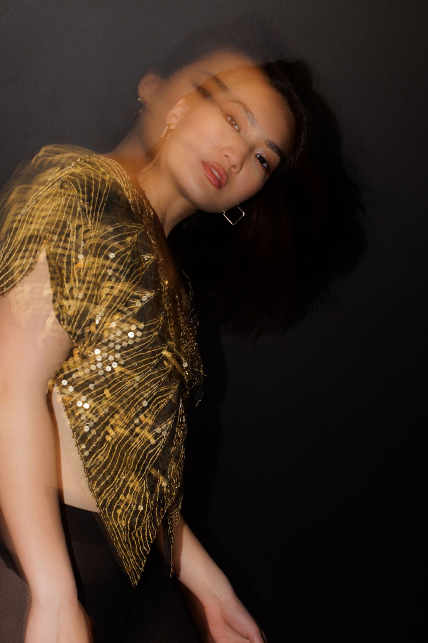Artistic portrait with tilted angle showing gold sequined fashion against dark background.