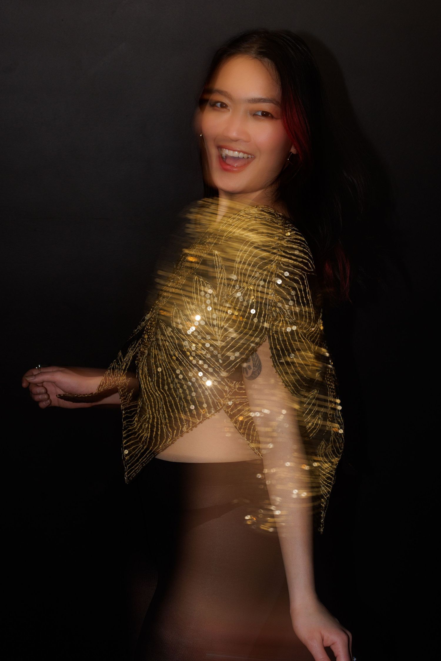 A person in a dazzling gold sequined top poses against a dark background with dynamic movement.
