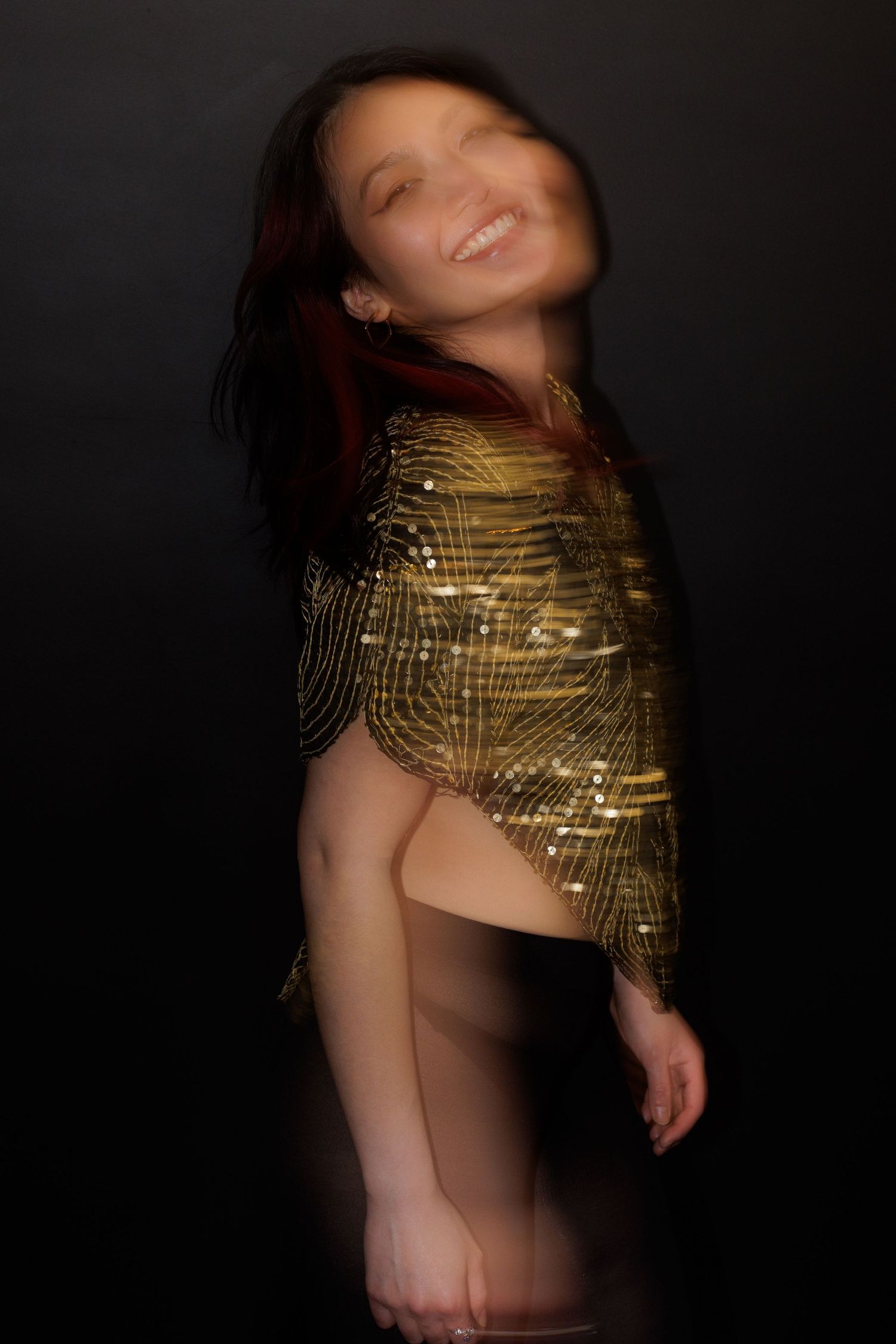 A joyful dance pose showcasing a sparkling gold top with blurred motion effects.