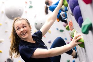 Rock climber in blue shirt scaling an indoor climbing wall with colorful holds.