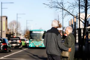 Two people standing on a city street with a turquoise bus visible in the background.