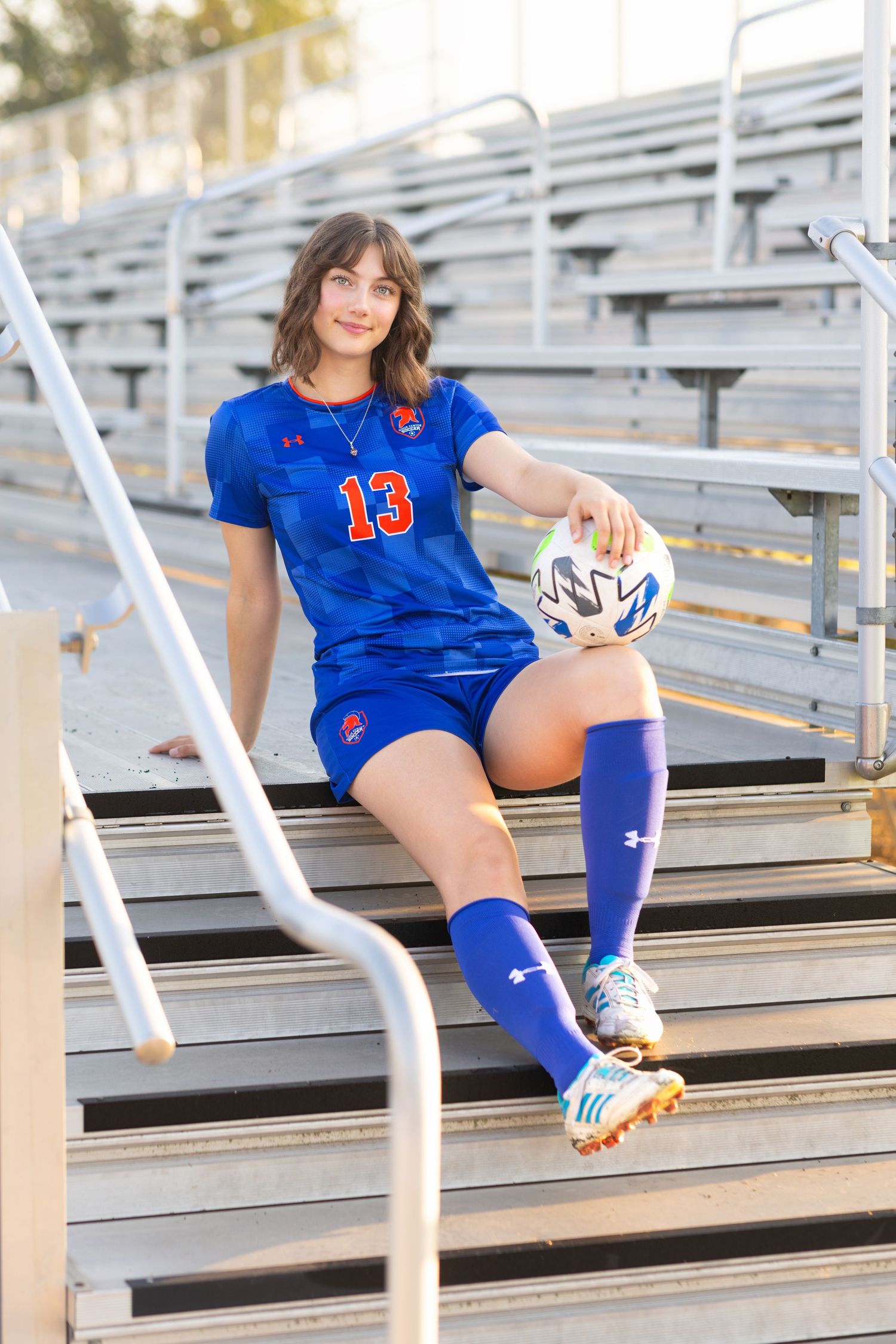 Senior portrait photographer photo of a senior sitting on bleachers holding a soccer ball on her knee. Photo take in Sioux Center, Iowa.