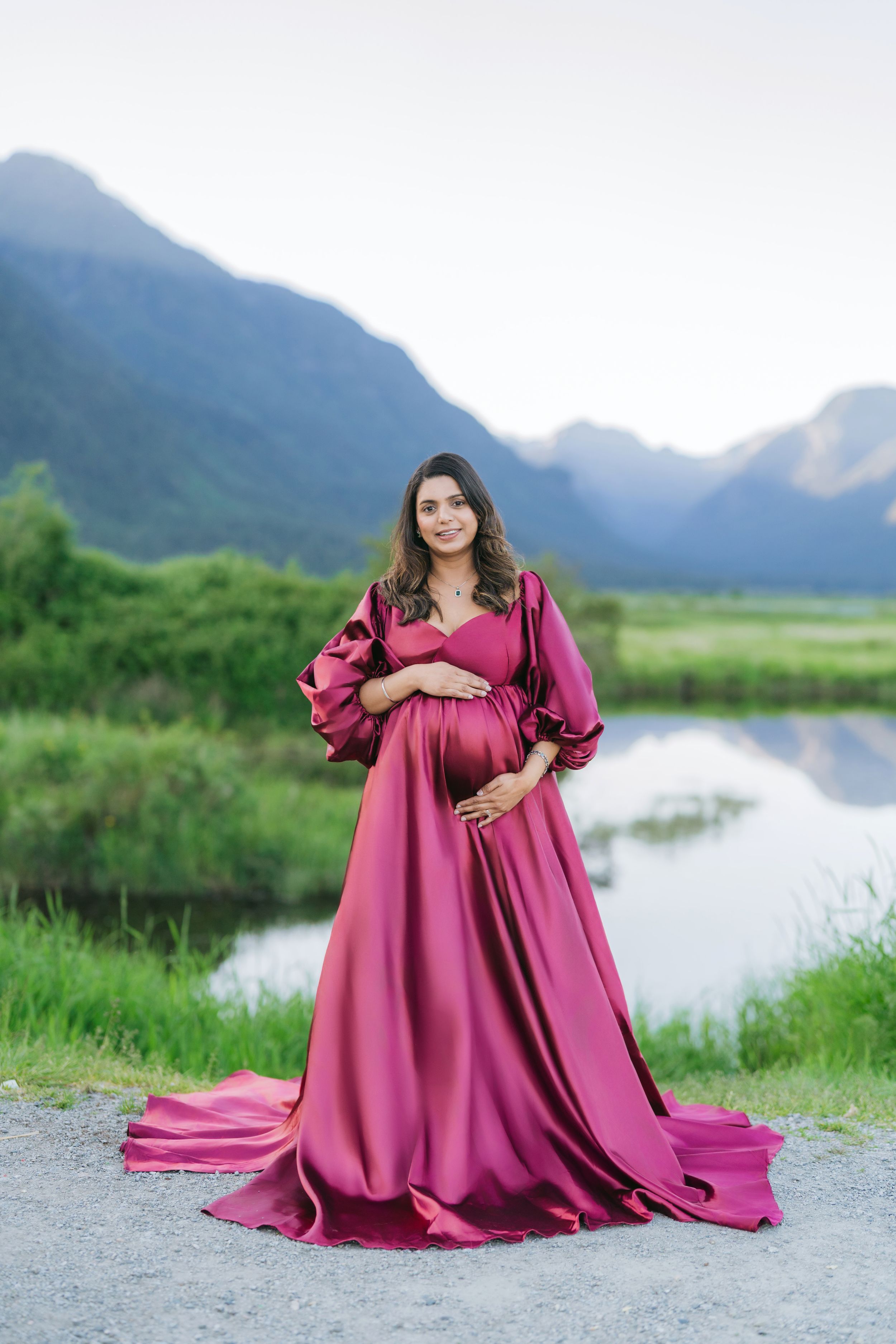 A flowing burgundy dress photographed against a scenic mountain lake landscape.