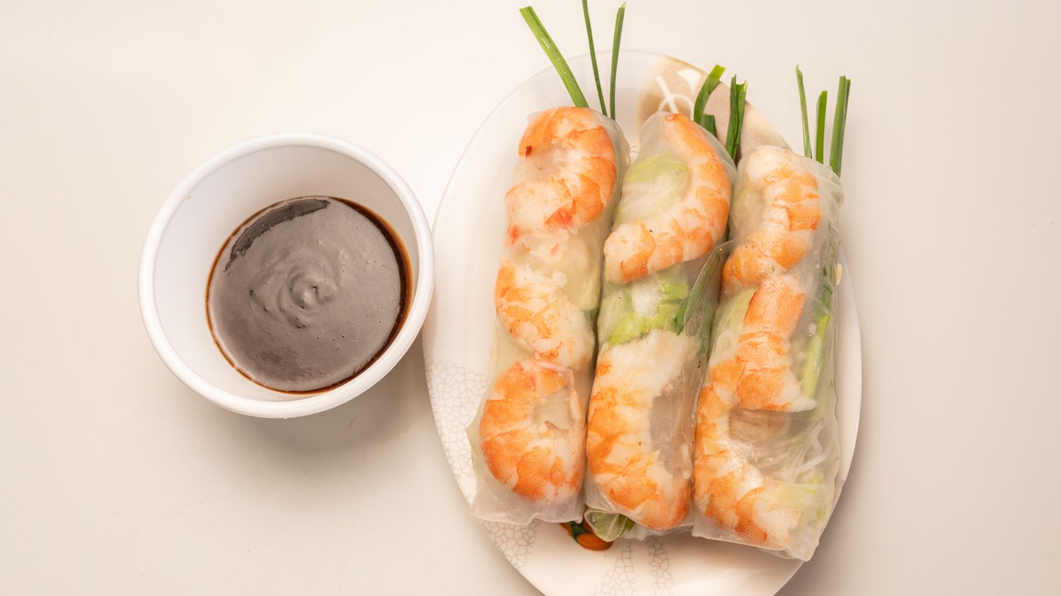 Fresh spring rolls with dipping sauce arranged on white background.