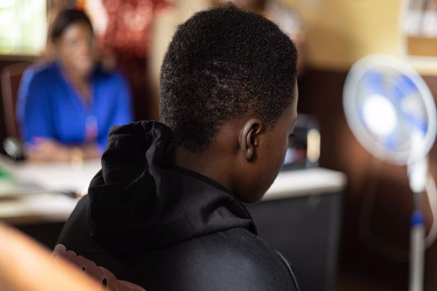 Back view of a person wearing a black hoodie in an office setting.