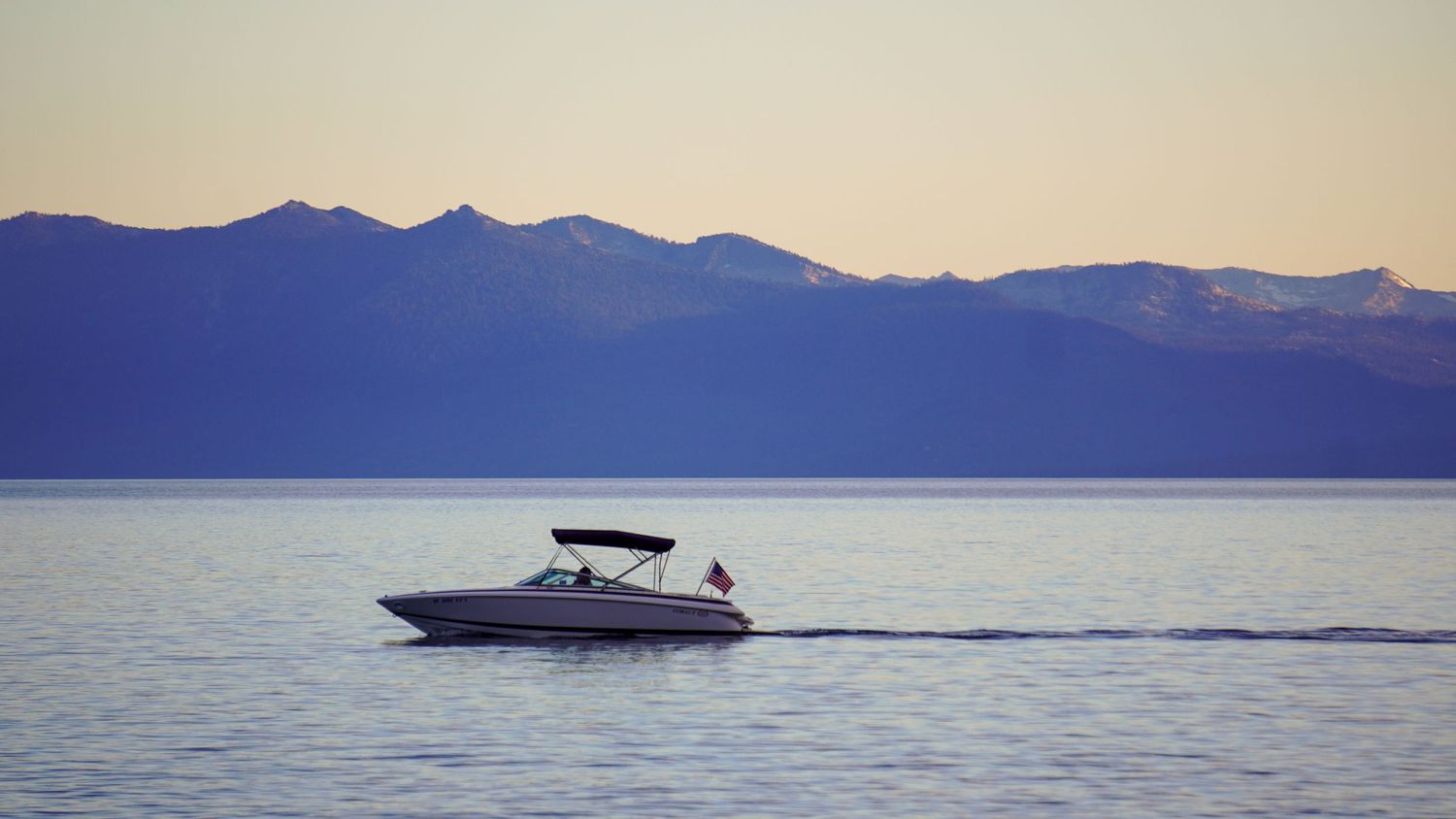 Scenic mountain lake view with boats and islands in the distance during sunset.