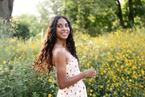 Elegant outdoor senior photo of a girl in a floral dress, smiling and standing in front of vibrant yellow spring flowers