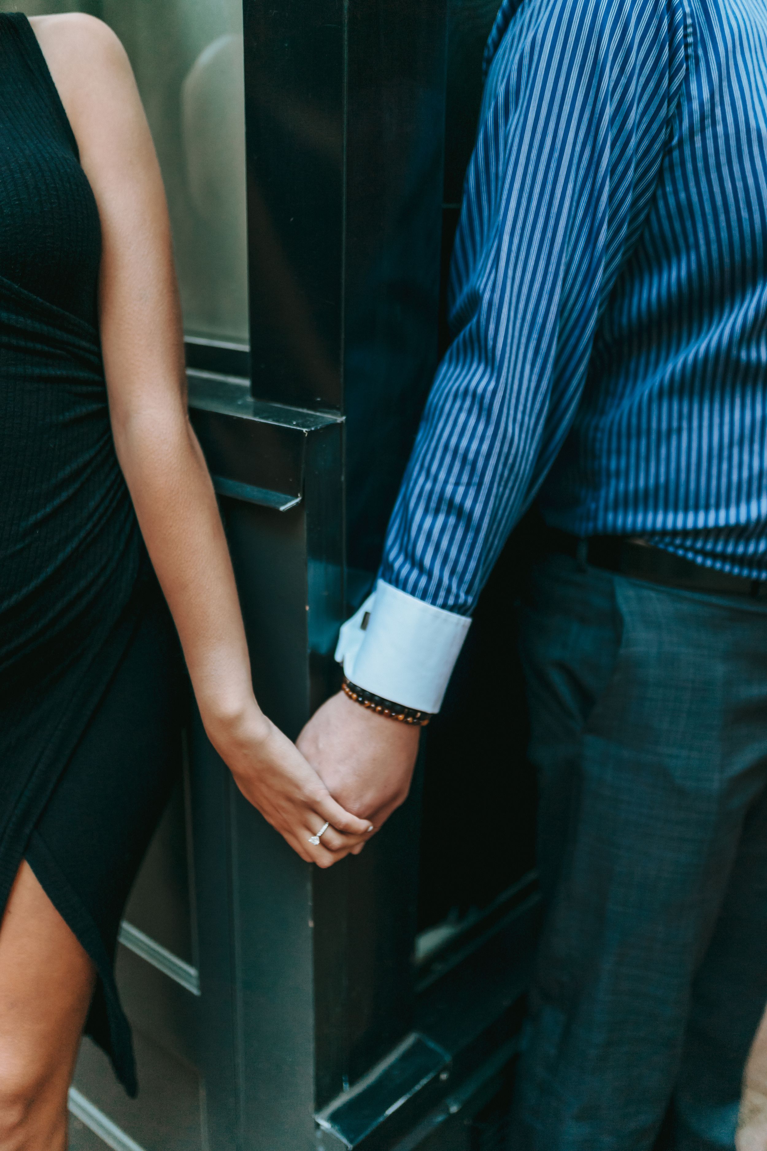Close-up of couple holding hands, with black dress and blue striped shirt visible.
