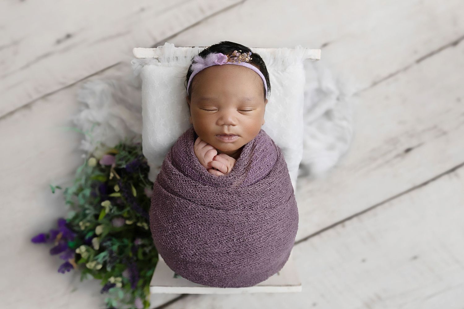 Image of baby girl in lilac purple lying in a white bed based in Coventry, Warwicks.