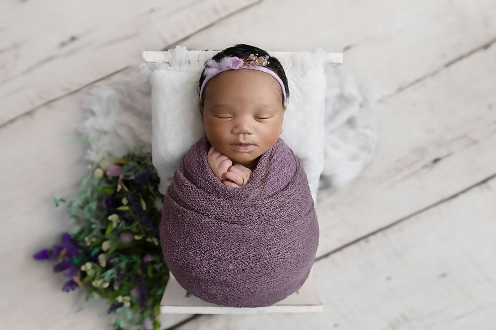 Image of baby girl in lilac purple lying in a white bed based in Coventry, Warwicks.