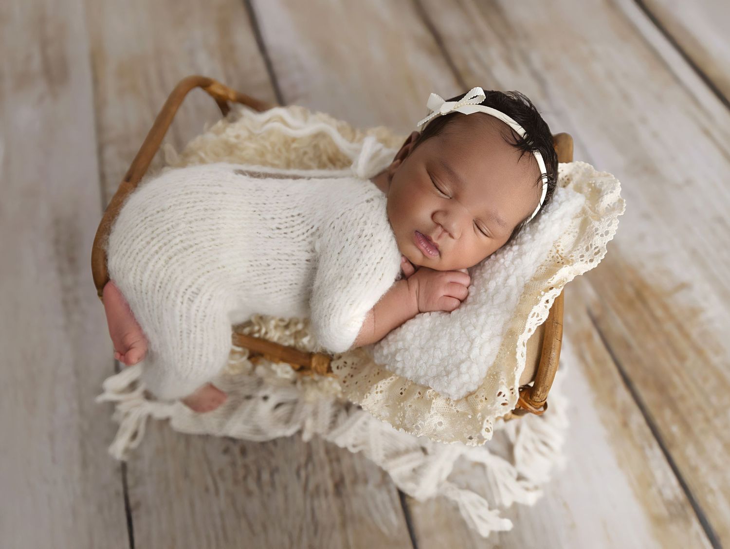 Image of newborn girl in a white fluffy romper  on a whicker basket Cane bed.