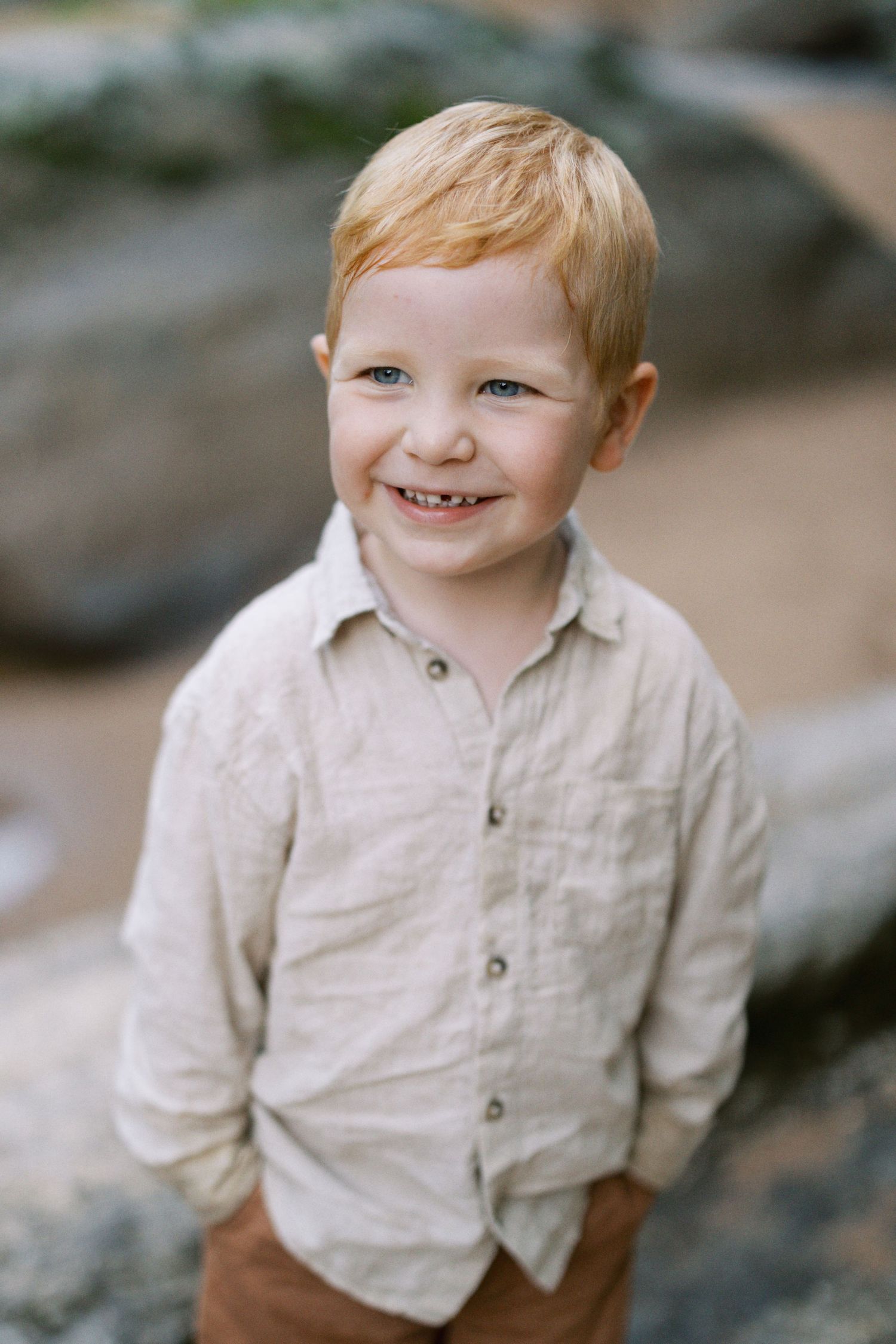 Cheerful young child wearing light colored button-up shirt smiles at camera outdoors.
