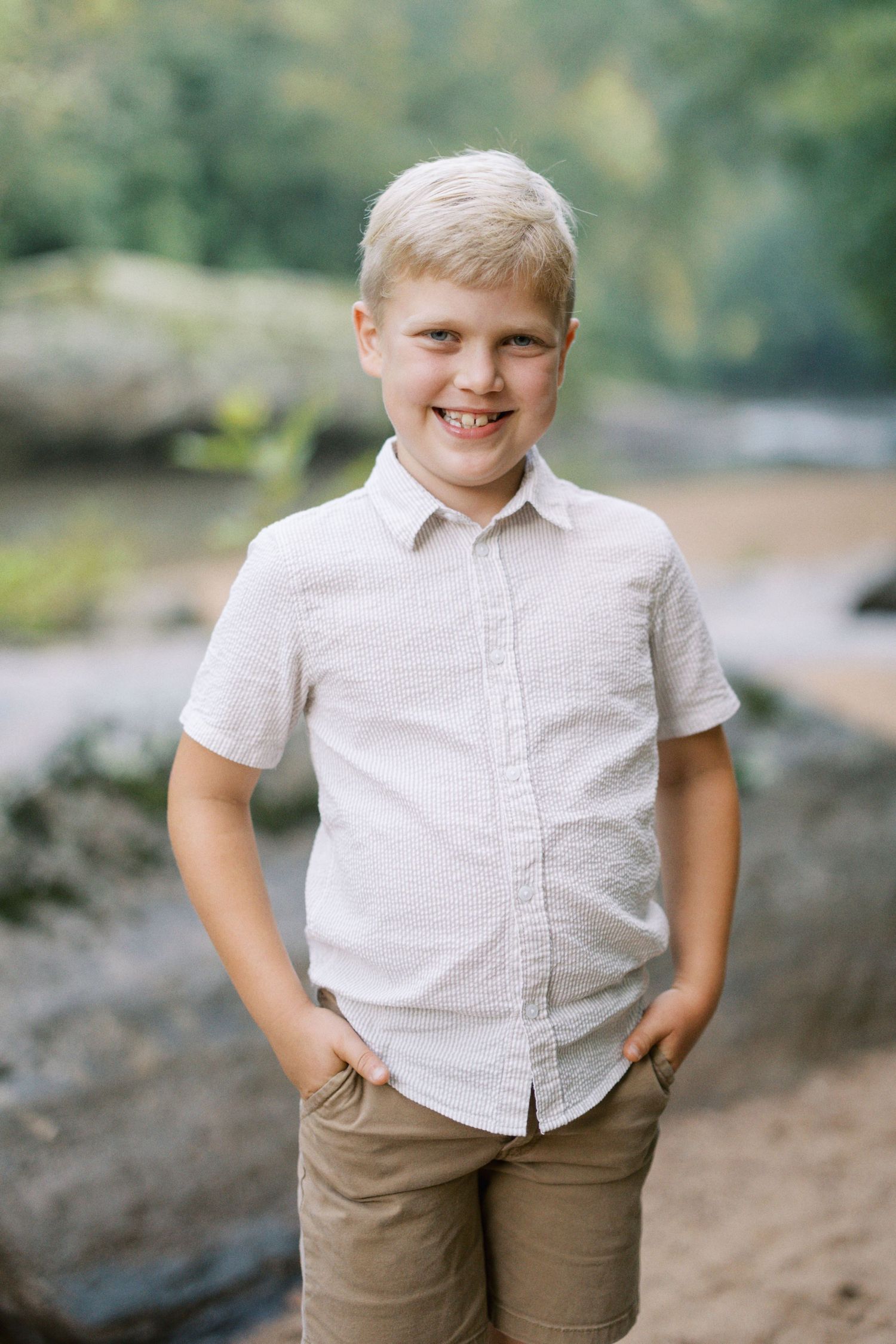 Child in white button-up shirt and khaki pants poses casually on nature trail.