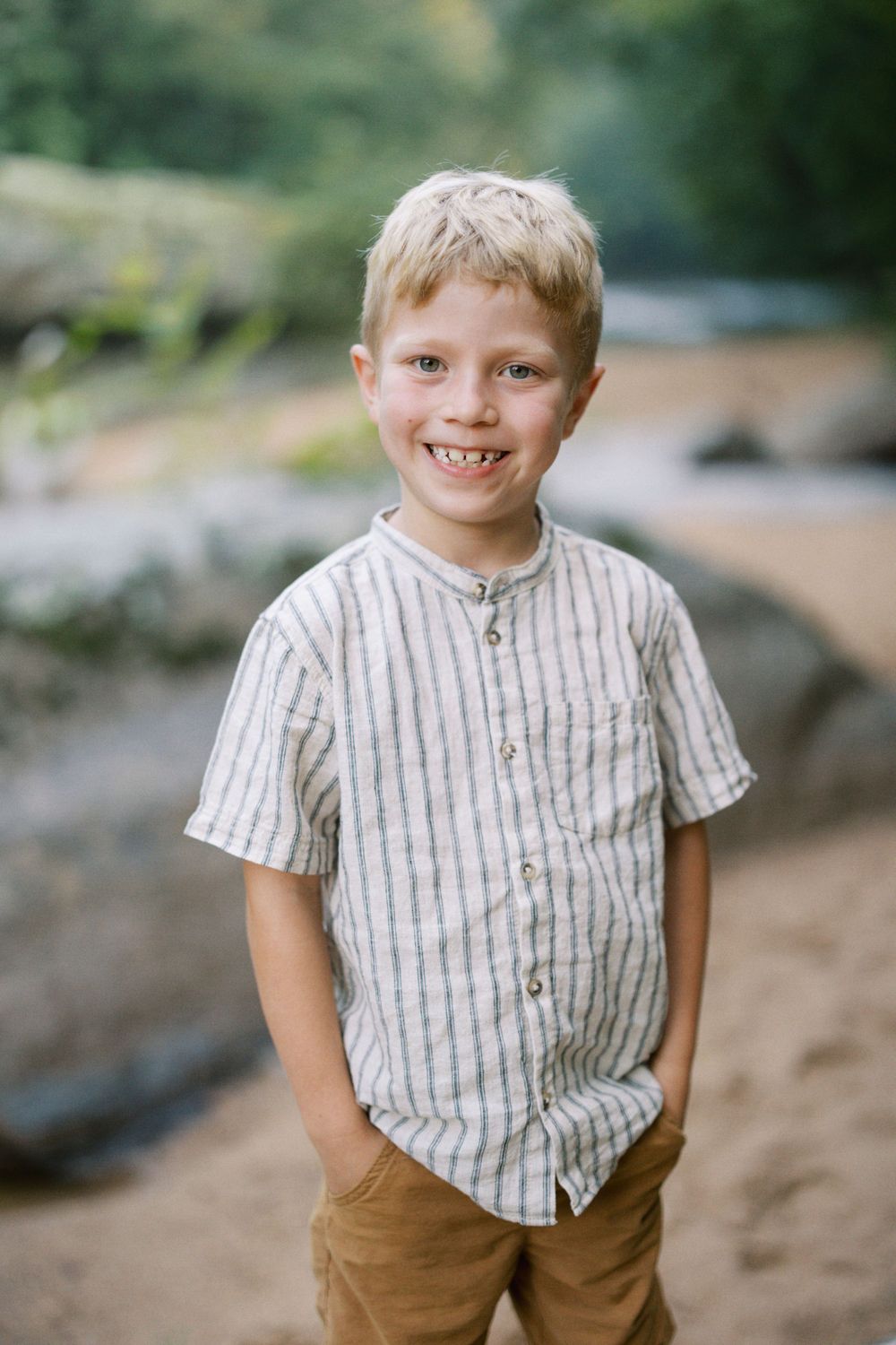 Child wearing striped button-up shirt smiles brightly while standing on outdoor path.