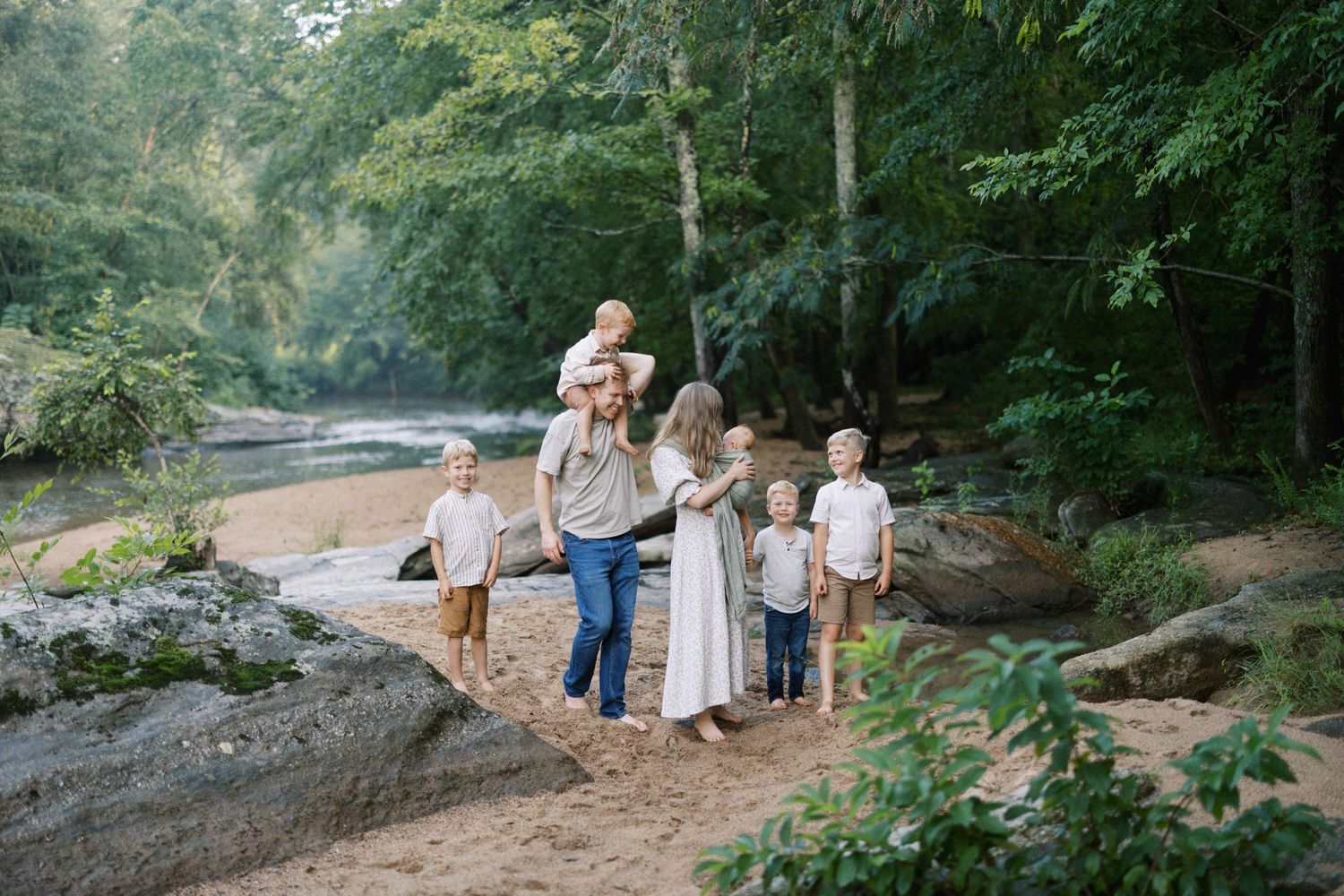 Family group stands together on rocky outcrop near river surrounded by green forest.