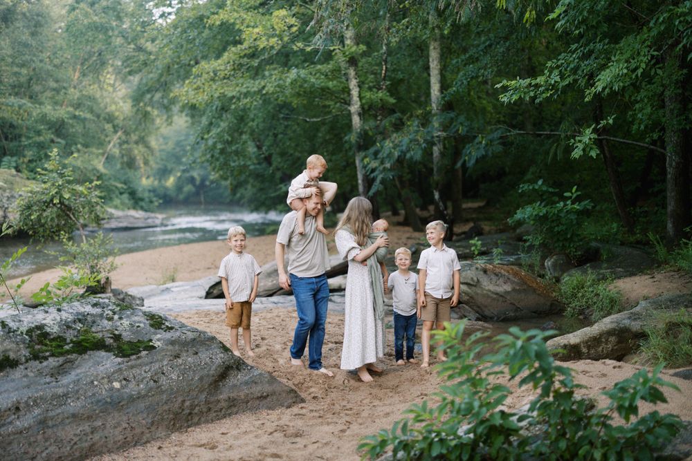 Family group stands together on rocky outcrop near river surrounded by green forest.