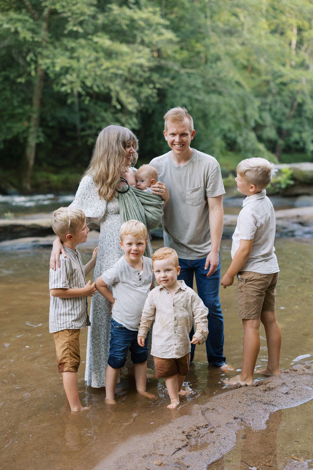 Family group stands together in shallow river water during outdoor photo session.