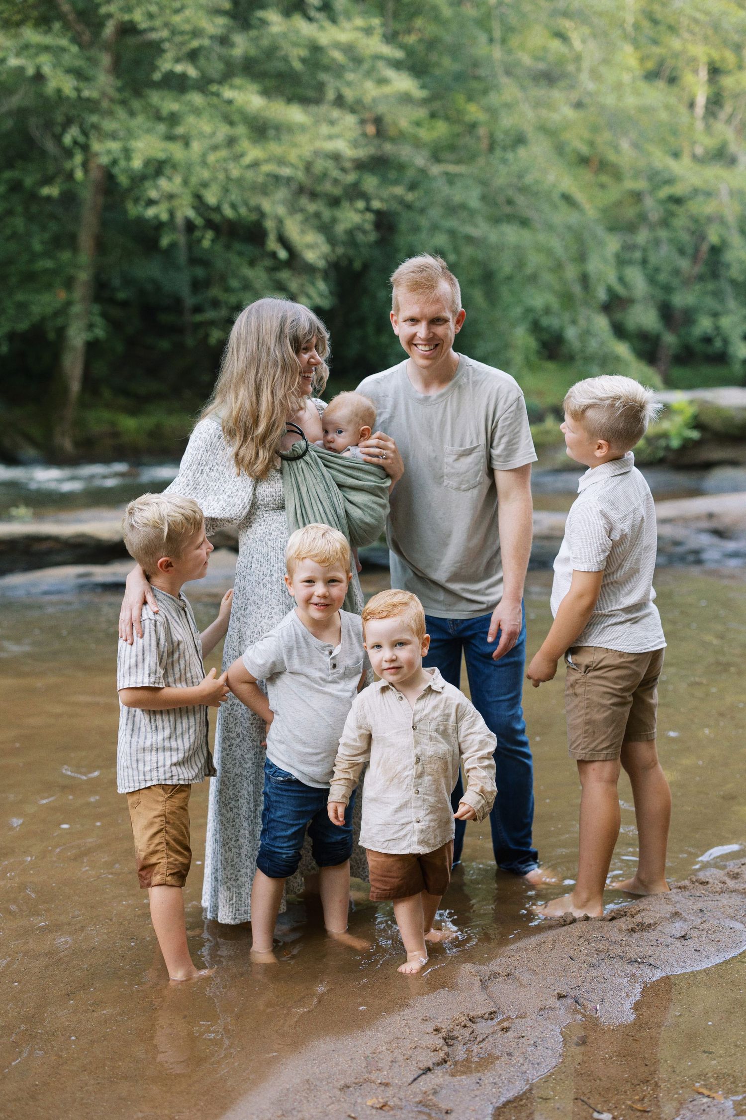 Family group stands together in shallow river water during outdoor photo session.