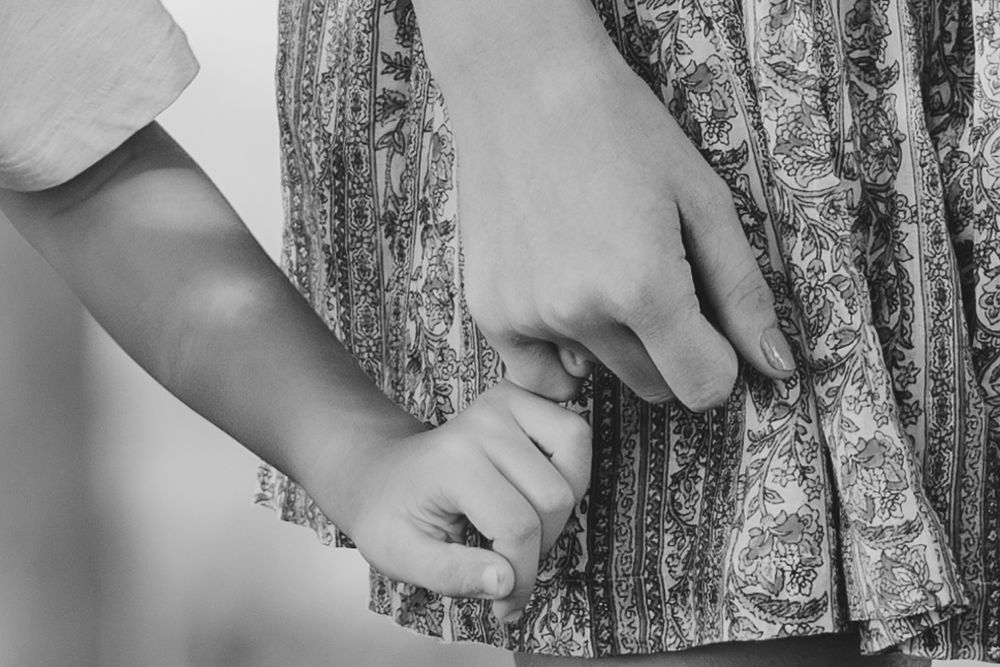 Close-up black and white image of hands holding fabric near a textured tree bark.