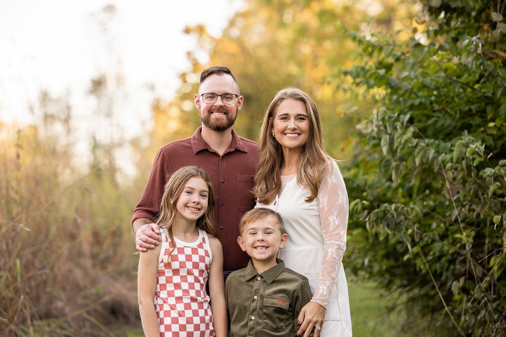 A family of four poses together outdoors in coordinated outfits during golden hour.