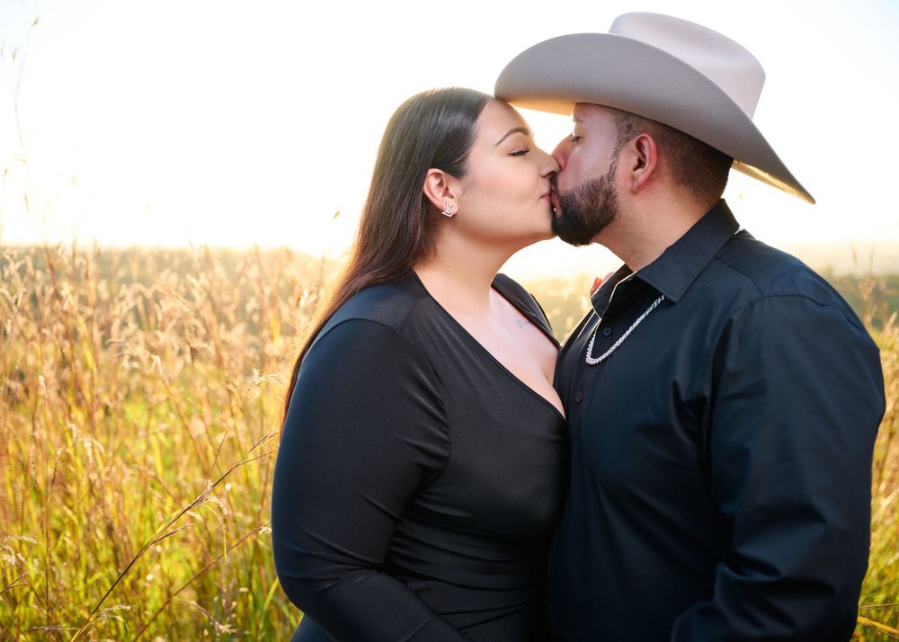 Couple in black outfits sharing romantic moment in golden field.