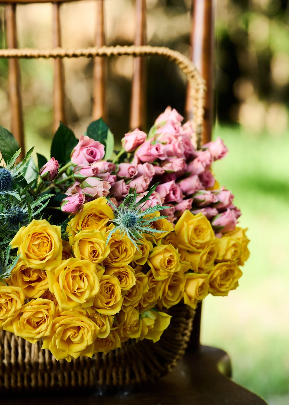 Beautiful arrangement of yellow roses and pink flowers in a rustic woven basket with natural outdoor background.