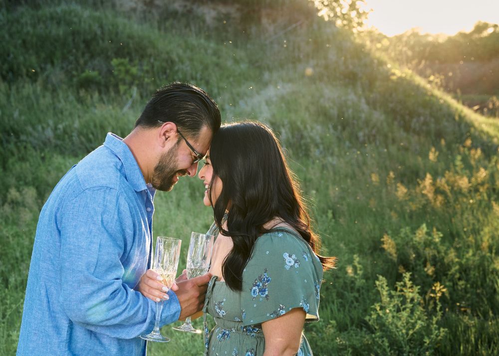 Two people holding wine glasses share an intimate moment in a sunlit meadow at golden hour.