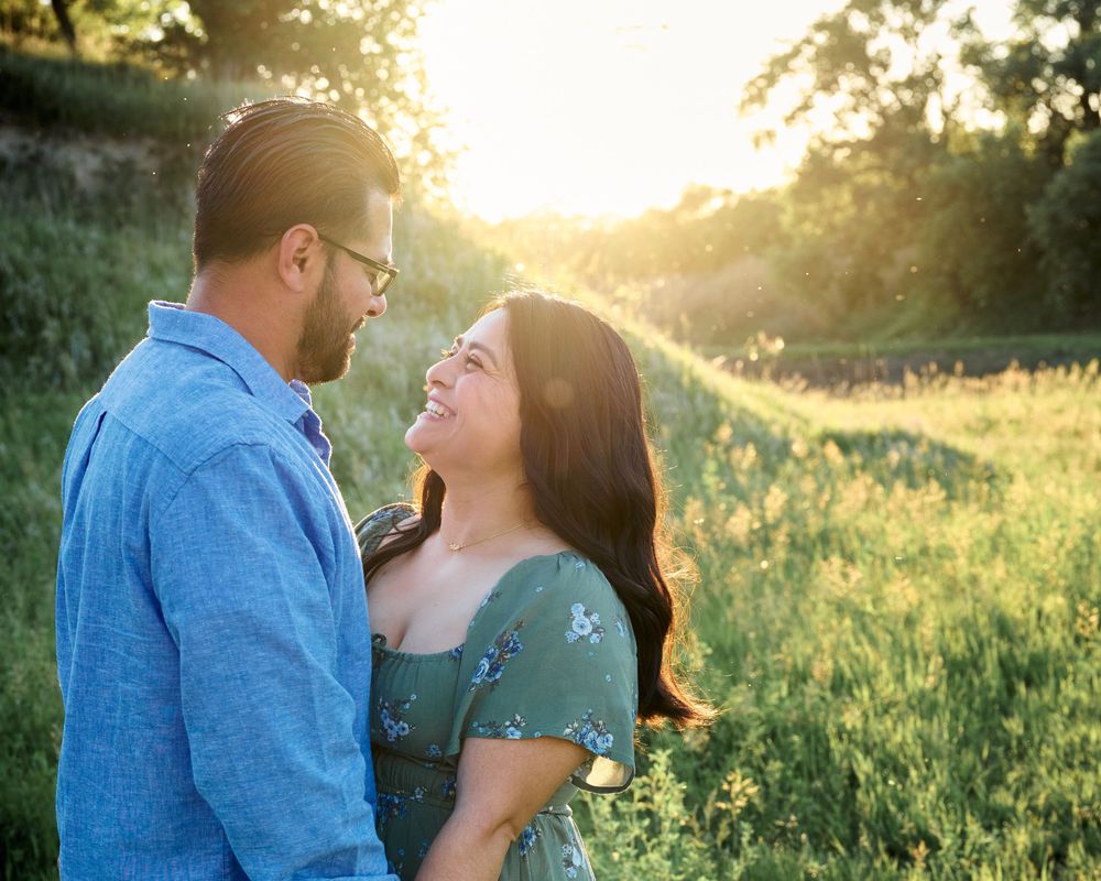Couple sharing romantic moment in sunlit meadow at golden hour with sun flare in background.