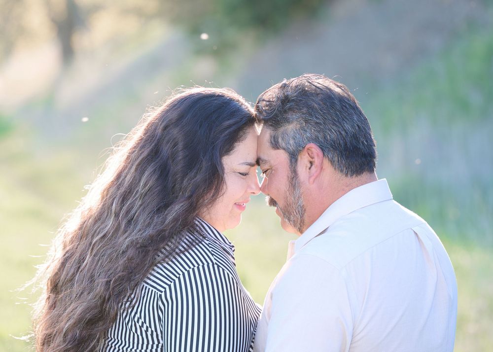 Intimate romantic moment captured in soft sunlight against natural outdoor backdrop.
