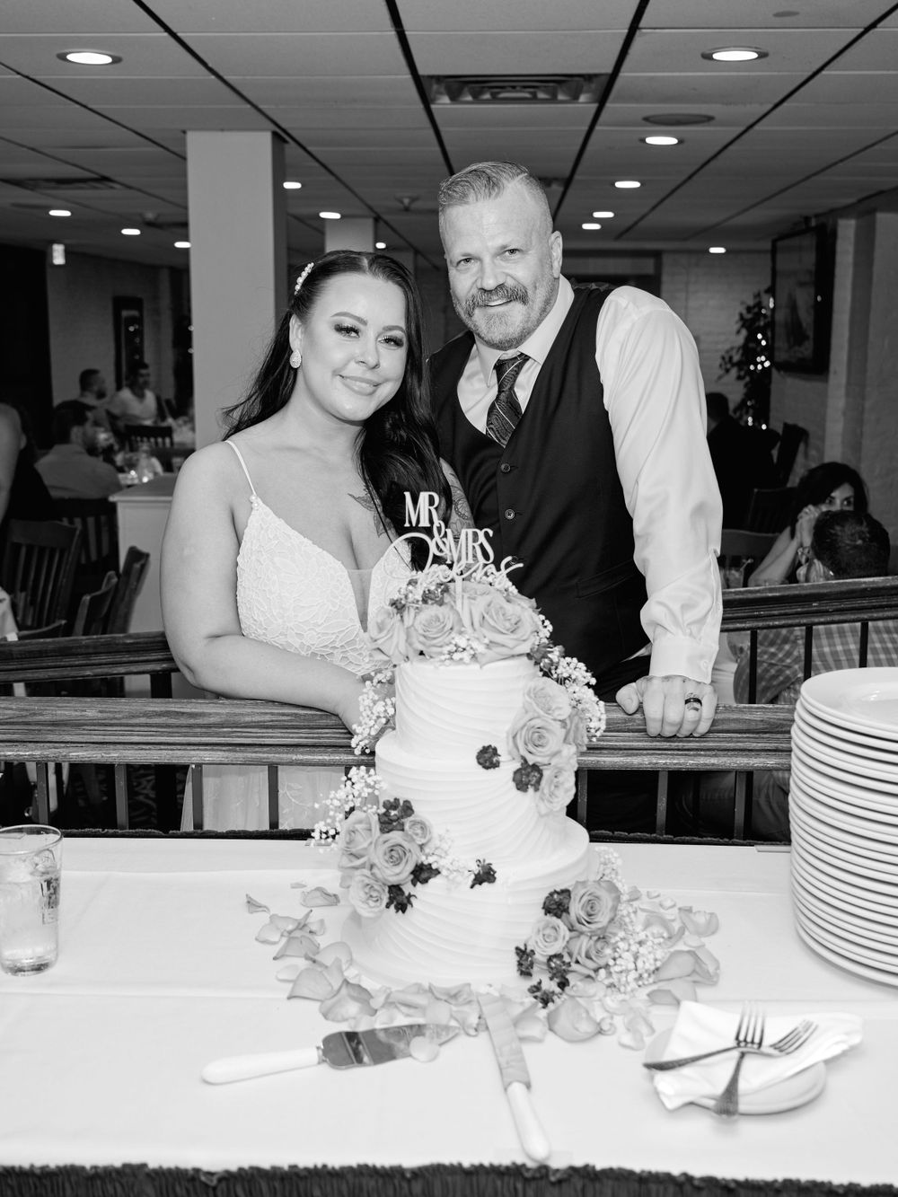 Black and white photo of newlyweds cutting their elegant three-tier wedding cake at reception.