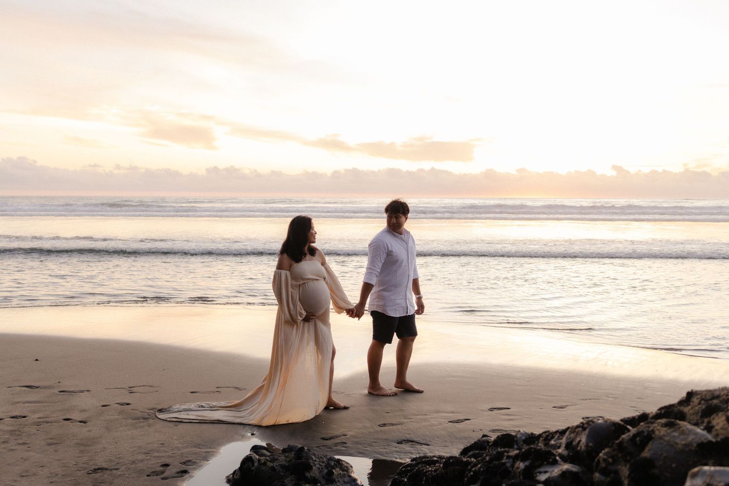 Couple walking along beach at sunset with flowing dress in romantic photoshoot.