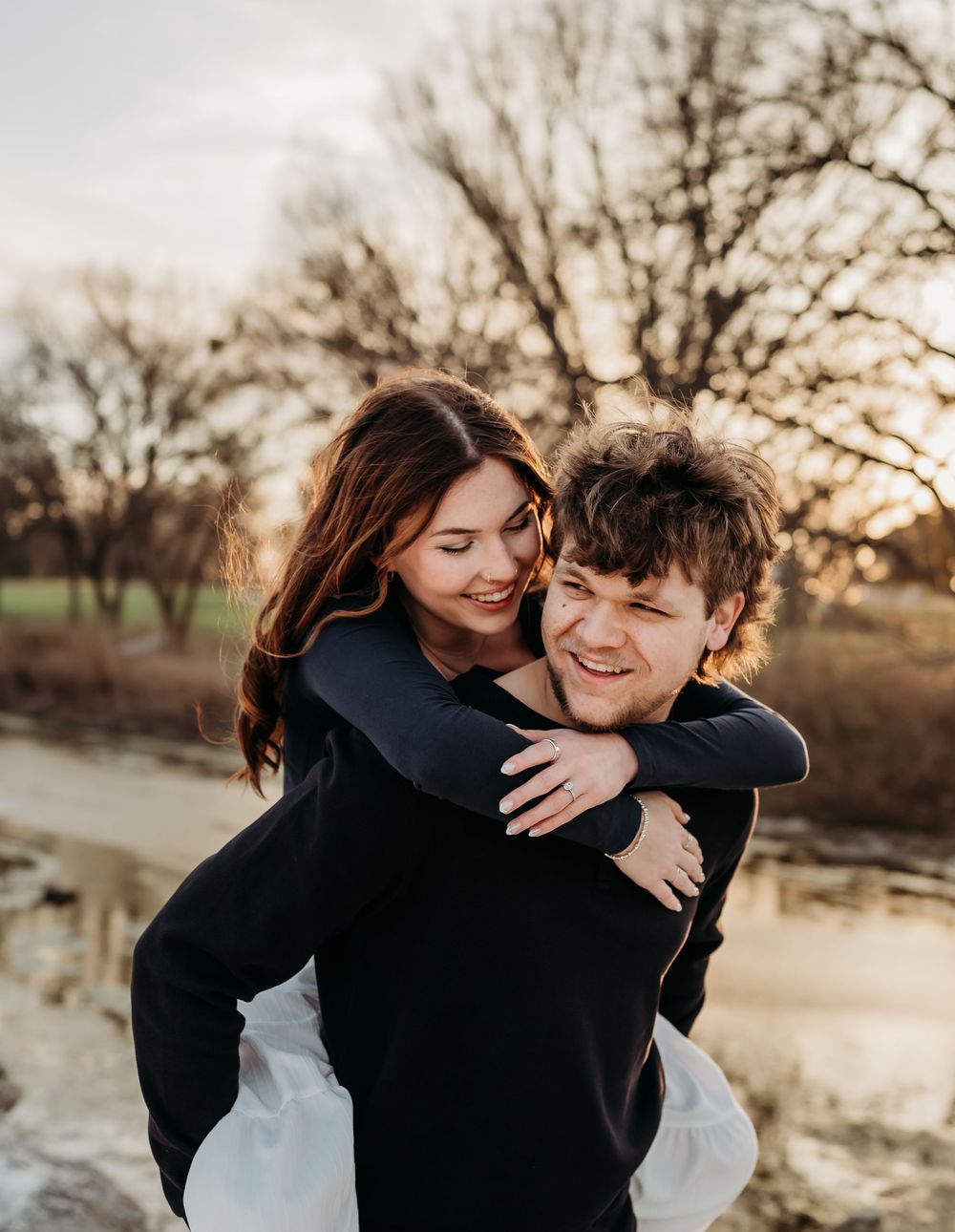 A couple shares intimate embraces and laughter during a romantic sunset photoshoot by a lake.
