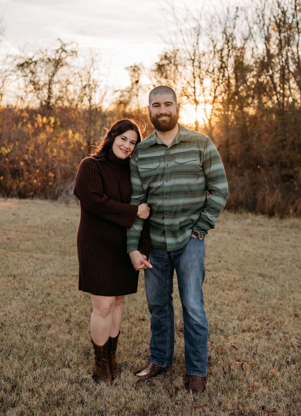 A couple shares a tender moment at sunset in a rustic field with golden light filtering through autumn trees.