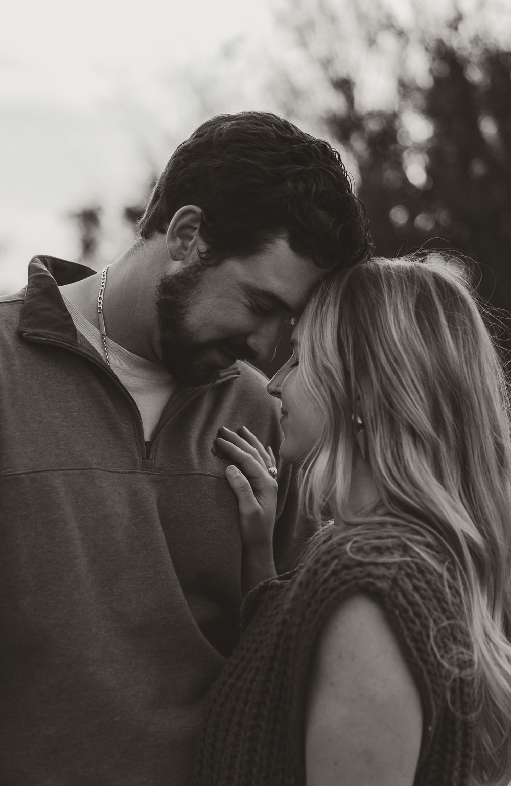 Black and white intimate portrait of a romantic couple sharing a tender moment outdoors.