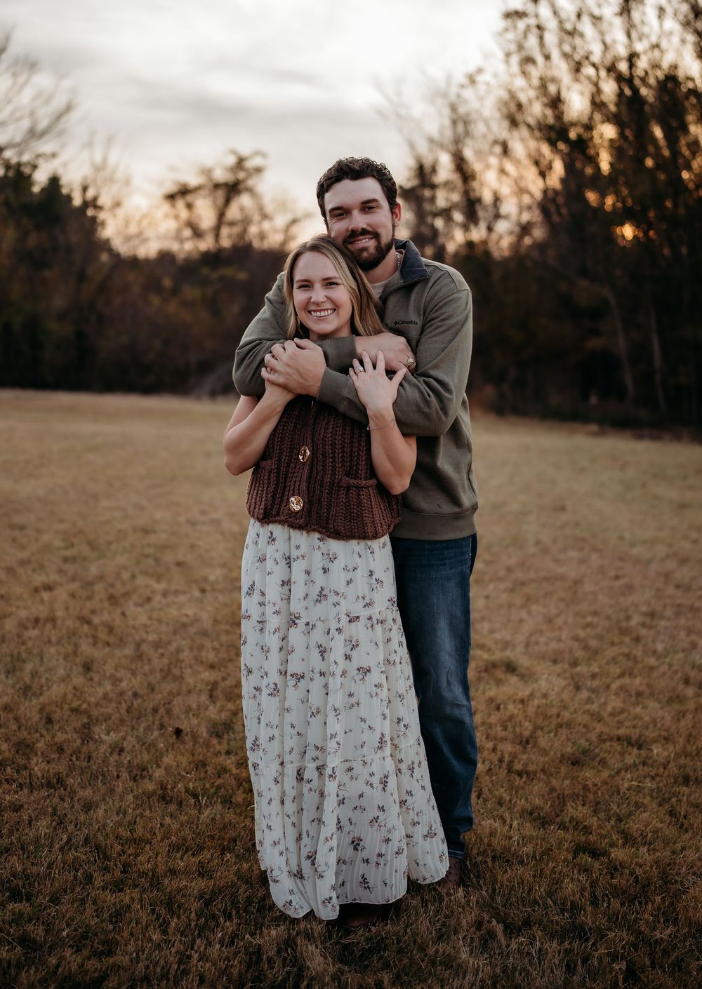 A couple embraces in a romantic sunset portrait session on a grassy field during golden hour.