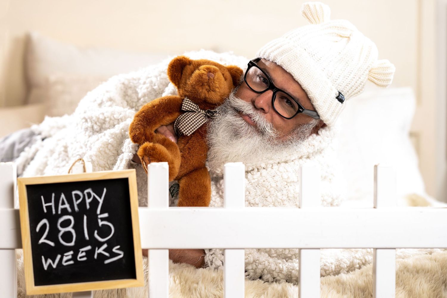 A teddy bear and chalkboard sign showing "Happy 23.15 weeks" sit in a white bed with soft blankets.